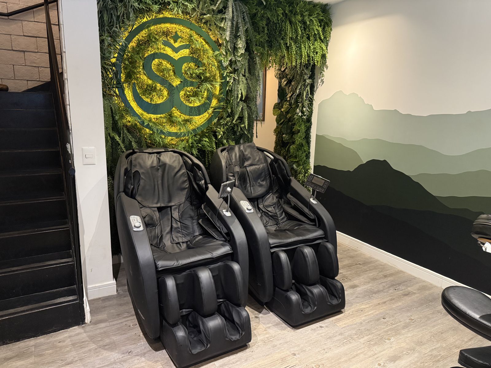 Duas poltronas de massagem pretas em frente ao jardim vertical com o símbolo Sense iluminado